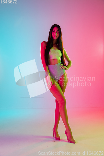 Image of Beautiful seductive girl in fashionable swimsuit on bright gradient pink-blue background in neon light