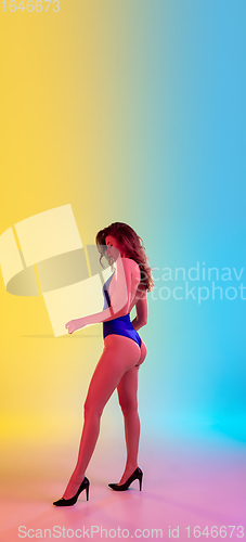 Image of Beautiful seductive girl in fashionable blue swimsuit on bright gradient yellow-blue background in neon light