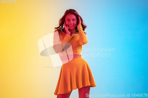 Image of Beautiful seductive girl in fashionable, romantic yellow outfit on bright gradient yellow-blue background in neon light