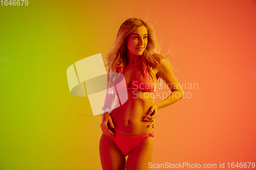 Image of Beautiful seductive girl in fashionable red swimsuit on bright gradient green-orange background in neon light