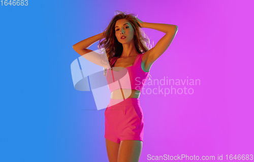 Image of Beautiful seductive girl in fashionable pink outfit on bright gradient purple-blue background in neon light