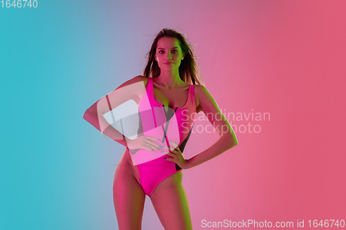 Image of Beautiful seductive girl in fashionable pink swimsuit on bright gradient pink-blue background in neon light