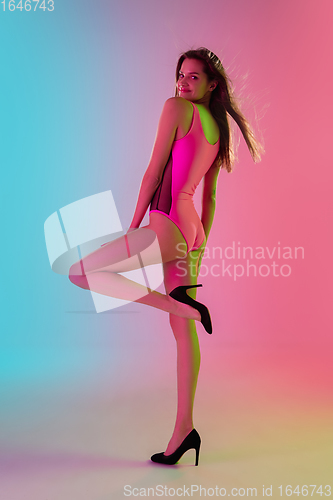 Image of Beautiful seductive girl in fashionable pink swimsuit on bright gradient pink-blue background in neon light