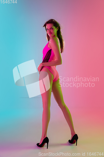 Image of Beautiful seductive girl in fashionable pink swimsuit on bright gradient pink-blue background in neon light