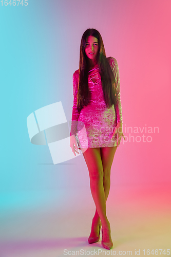 Image of Beautiful seductive girl in fashionable dress, outfit on bright gradient pink-blue background in neon light