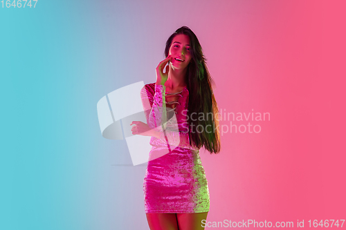 Image of Beautiful seductive girl in fashionable dress, outfit on bright gradient pink-blue background in neon light