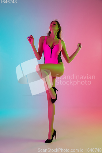 Image of Beautiful seductive girl in fashionable pink swimsuit on bright gradient pink-blue background in neon light