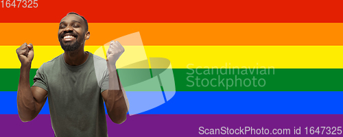 Image of Young astonished african-american man on multicolored background forming a pride flag