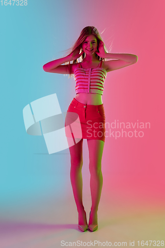 Image of Beautiful girl in fashionable, romantic outfit on bright gradient pink-blue background in neon light