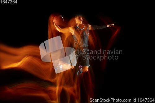 Image of Young east asian basketball player in action and jump in mixed light over dark studio background. Concept of sport, movement, energy and dynamic, healthy lifestyle.