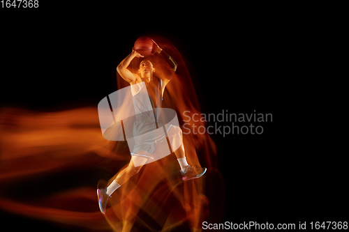 Image of Young east asian basketball player in action and jump in mixed light over dark studio background. Concept of sport, movement, energy and dynamic, healthy lifestyle.