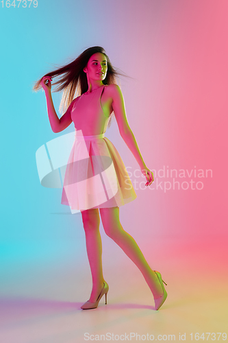 Image of Beautiful seductive girl in fashionable, romantic outfit on bright gradient pink-blue background in neon light
