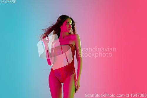 Image of Beautiful seductive girl in fashionable red swimsuit on bright gradient pink-blue background in neon light