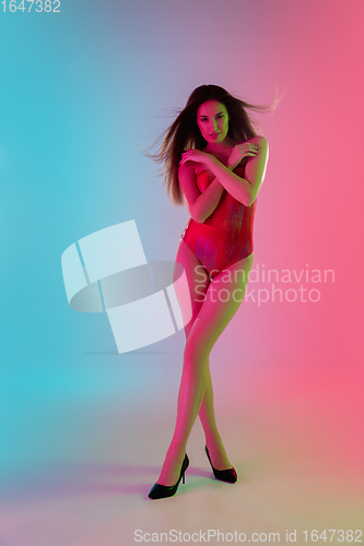 Image of Beautiful seductive girl in fashionable red swimsuit on bright gradient pink-blue background in neon light