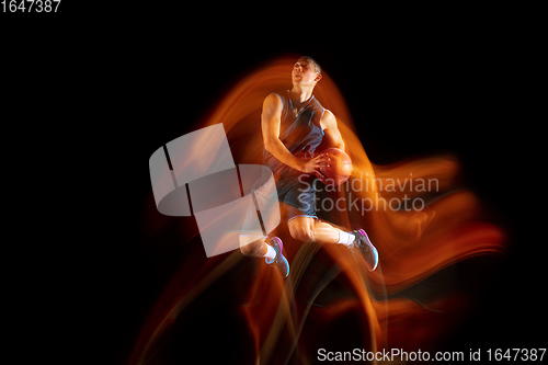 Image of Young east asian basketball player in action and jump in mixed light over dark studio background. Concept of sport, movement, energy and dynamic, healthy lifestyle.