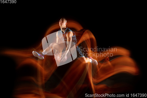 Image of Young east asian basketball player in action and jump in mixed light over dark studio background. Concept of sport, movement, energy and dynamic, healthy lifestyle.