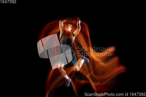 Image of Young east asian basketball player in action and jump in mixed light over dark studio background. Concept of sport, movement, energy and dynamic, healthy lifestyle.