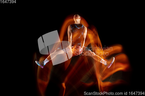 Image of Young east asian basketball player in action and jump in mixed light over dark studio background. Concept of sport, movement, energy and dynamic, healthy lifestyle.