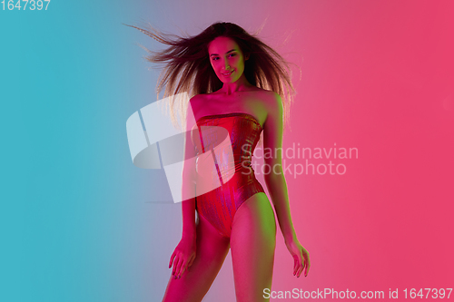 Image of Beautiful seductive girl in fashionable red swimsuit on bright gradient pink-blue background in neon light