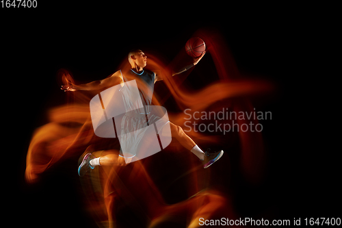 Image of Young east asian basketball player in action and jump in mixed light over dark studio background. Concept of sport, movement, energy and dynamic, healthy lifestyle.