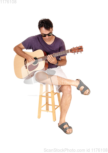 Image of Young man sitting and playing his guitar