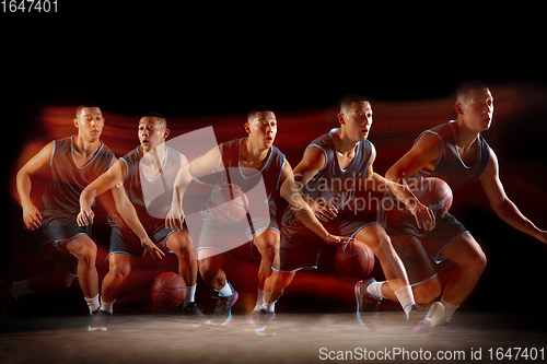 Image of Young east asian basketball player in action and jump in mixed strobe light over dark studio background. Concept of sport, movement, energy and dynamic, healthy lifestyle.