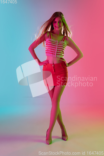 Image of Beautiful girl in fashionable, romantic outfit on bright gradient pink-blue background in neon light