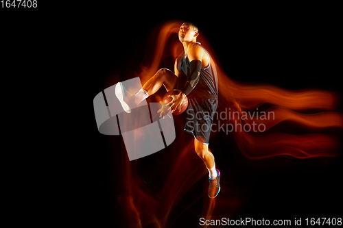 Image of Young east asian basketball player in action and jump in mixed light over dark studio background. Concept of sport, movement, energy and dynamic, healthy lifestyle.