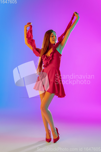 Image of Beautiful happy girl in fashionable, romantic outfit on bright gradient purple-blue background in neon light