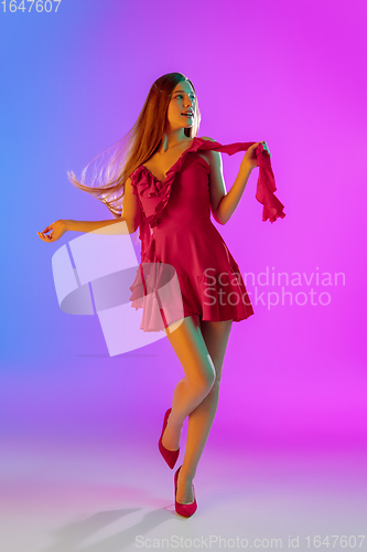 Image of Beautiful happy girl in fashionable, romantic outfit on bright gradient purple-blue background in neon light