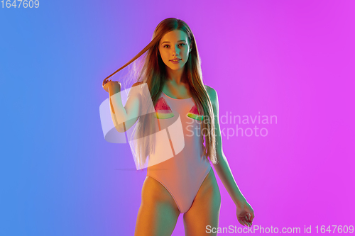 Image of Beautiful seductive girl in fashionable pink swimsuit on bright gradient purple-blue background in neon light