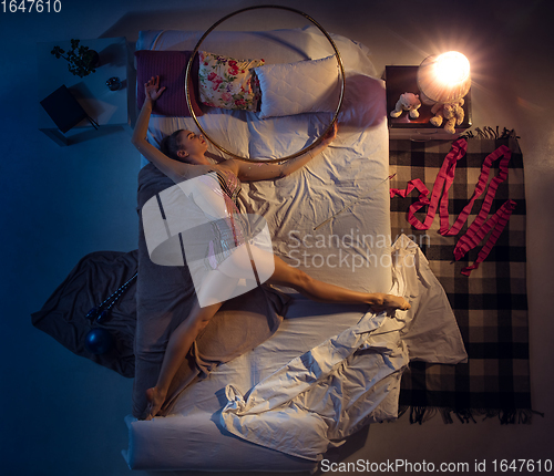 Image of Top view of young professional rhythmic gymnast sleeping at her bedroom in sportwear. Home interior.