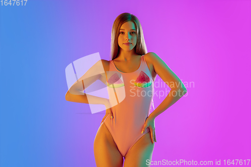 Image of Beautiful seductive girl in fashionable pink swimsuit on bright gradient purple-blue background in neon light