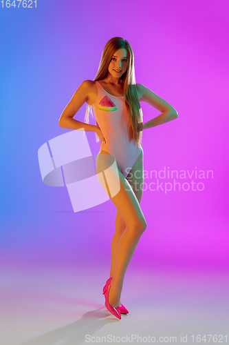 Image of Beautiful seductive girl in fashionable pink swimsuit on bright gradient purple-blue background in neon light