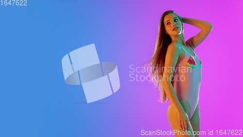 Image of Beautiful seductive girl in fashionable pink swimsuit on bright gradient purple-blue background in neon light