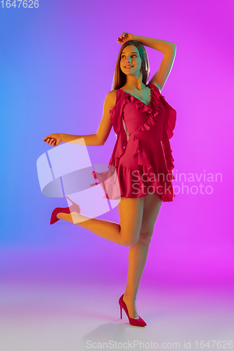 Image of Beautiful happy girl in fashionable, romantic outfit on bright gradient purple-blue background in neon light