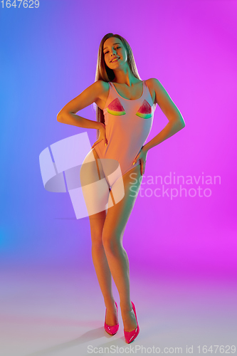 Image of Beautiful seductive girl in fashionable pink swimsuit on bright gradient purple-blue background in neon light