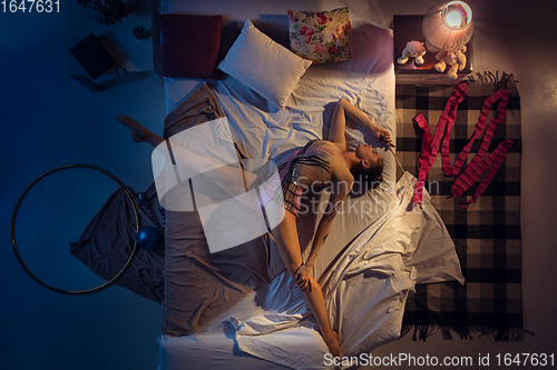 Image of Top view of young professional rhythmic gymnast sleeping at her bedroom in sportwear. Home interior.