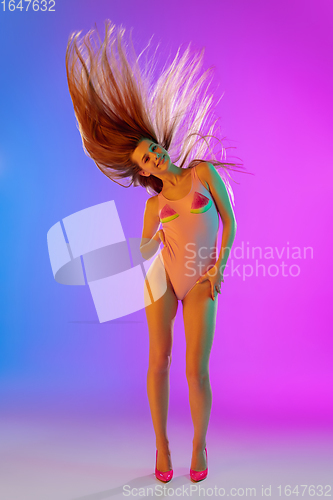 Image of Beautiful seductive girl in fashionable pink swimsuit on bright gradient purple-blue background in neon light