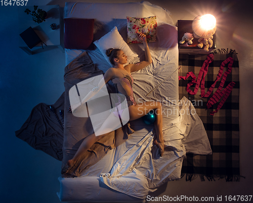 Image of Top view of young professional rhythmic gymnast sleeping at her bedroom in sportwear with blue ball.