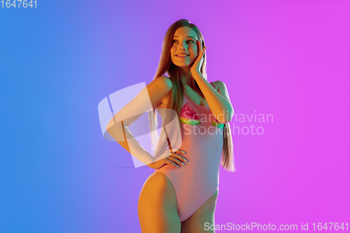 Image of Beautiful seductive girl in fashionable pink swimsuit on bright gradient purple-blue background in neon light