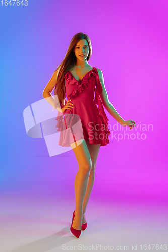 Image of Beautiful happy girl in fashionable, romantic outfit on bright gradient purple-blue background in neon light