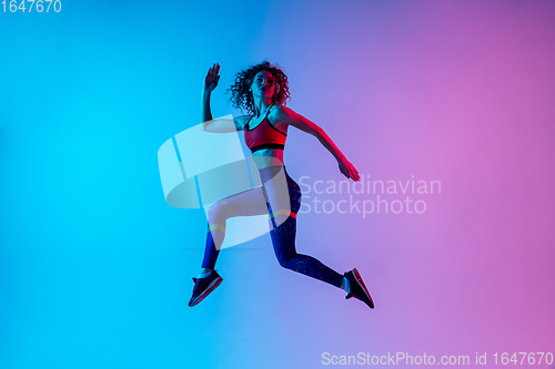 Image of Young beautiful woman in bright sportwear isolated on gradient pink-blue studio background in neon light.