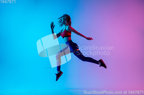 Image of Young sportive woman running isolated on gradient pink-blue studio background in neon light.