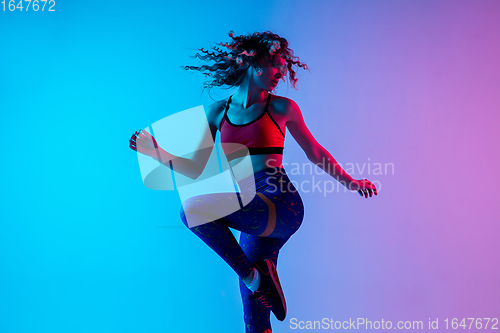 Image of Sportive young happy woman in bright sportwear isolated on gradient pink-blue studio background in neon light.