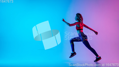 Image of Young sportive woman running isolated on gradient pink-blue studio background in neon light.