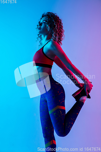 Image of Young sportive woman training isolated on gradient pink-blue studio background in neon light.