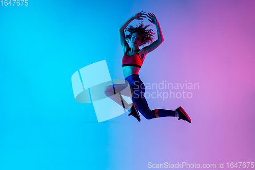 Image of Portrait of young beautiful woman in bright sportwear isolated on gradient pink-blue studio background in neon light.