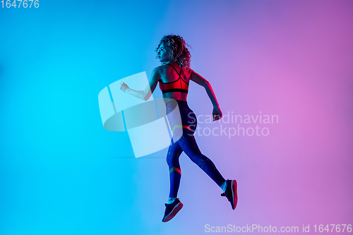 Image of Young sportive woman running isolated on gradient pink-blue studio background in neon light.