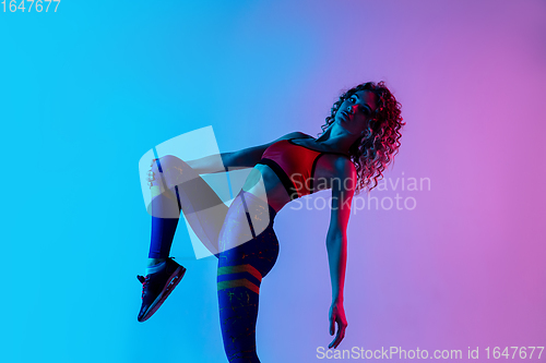 Image of Portrait of young beautiful woman in bright sportwear isolated on gradient pink-blue studio background in neon light.